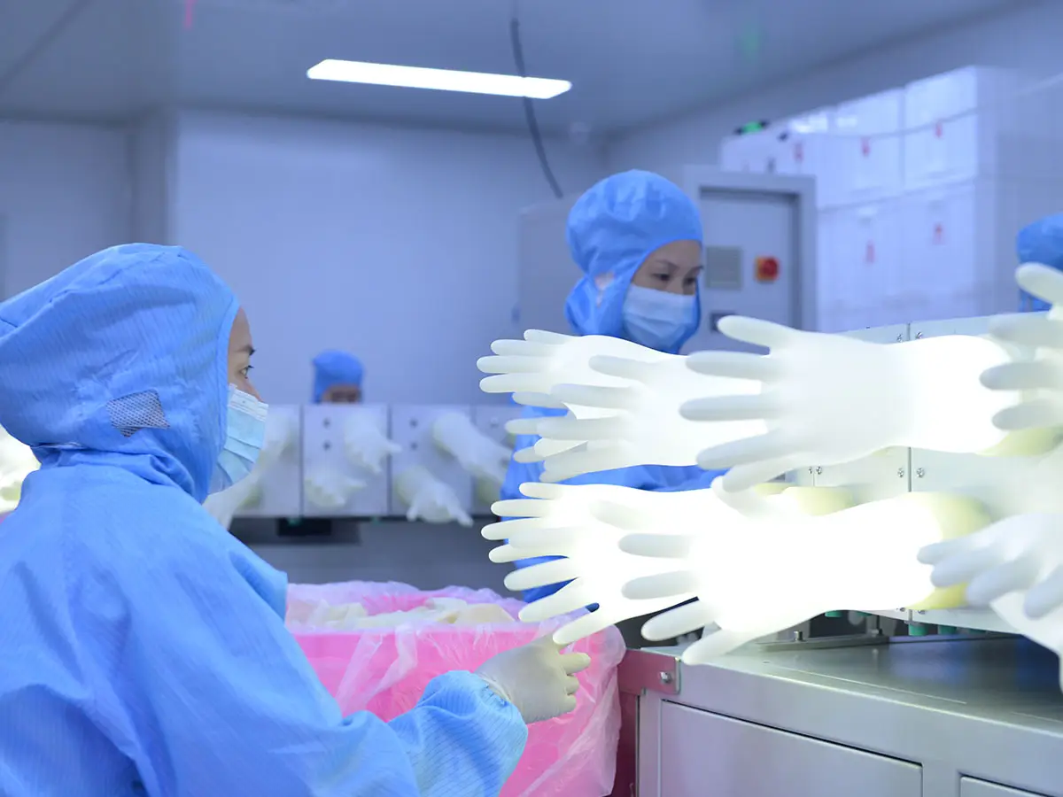 QC inspectors in cleanroom suits visually inspecting surgical gloves on automated production line