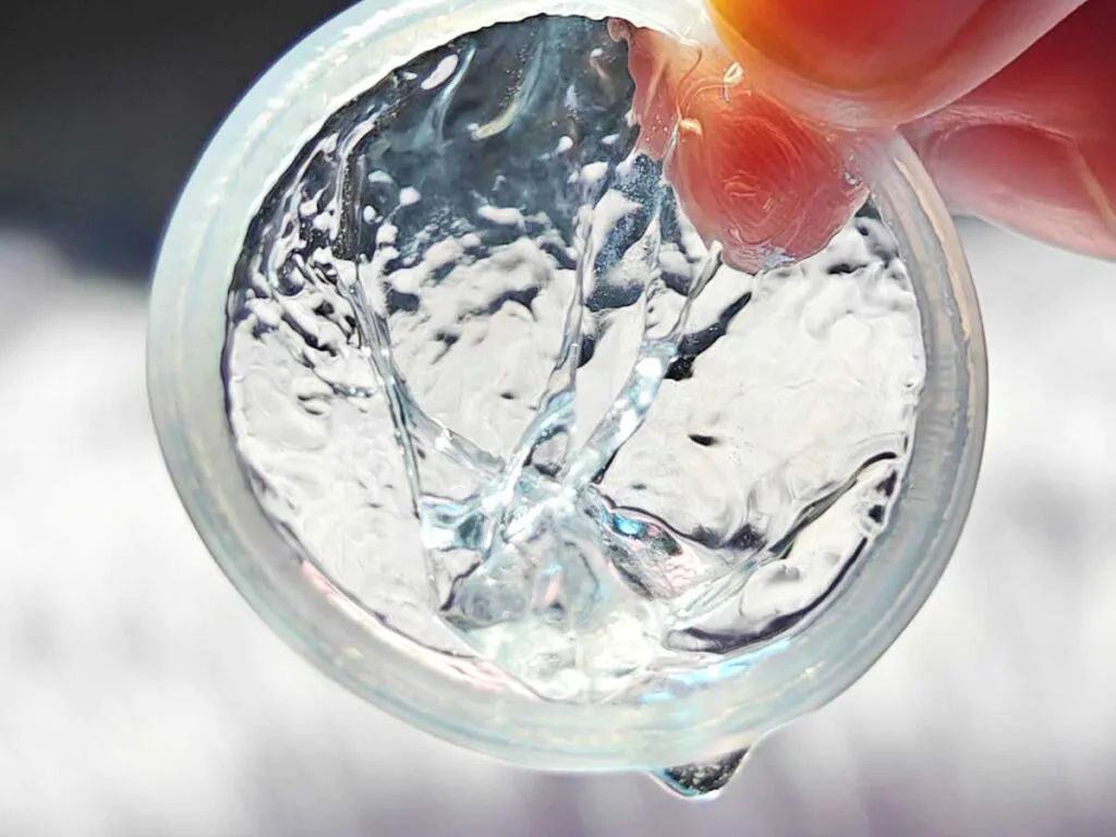 Close-up of a transparent polyurethane condom held between fingers, showing its rolled rim and lubricated surface.