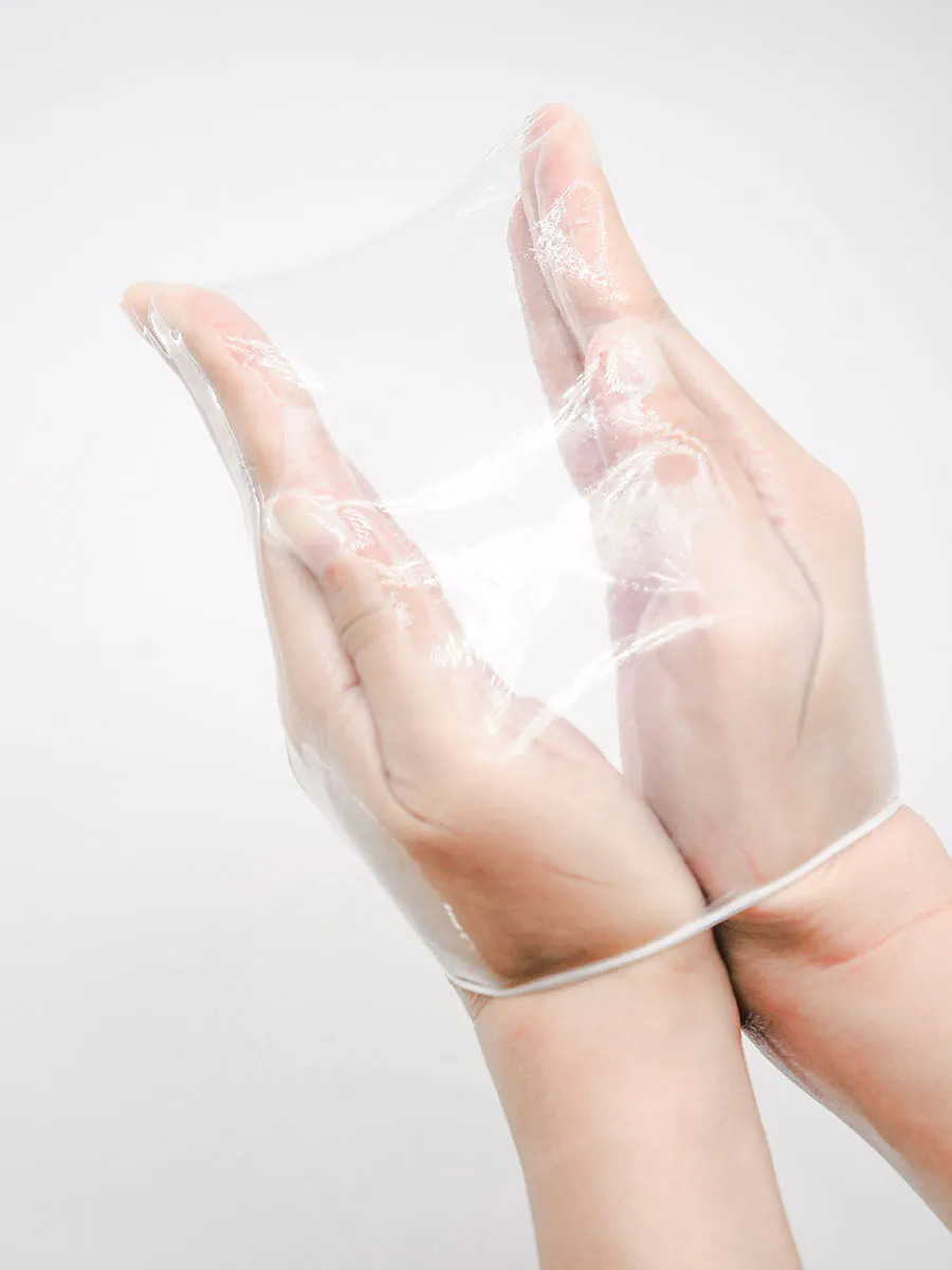 Hands stretching a transparent BENOW polyurethane condom against a white background.
